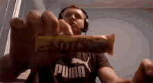 a man wearing headphones and a puma shirt is holding a snickers bar .