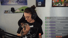 a woman wearing headphones holds a kitten in front of a poster for star wars