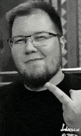 a man with glasses and a beard is pointing at his face