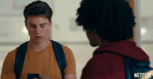 a man looking at his phone next to another man with a netflix logo on his backpack