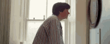 a man in a striped shirt is looking at a mirror in a room .