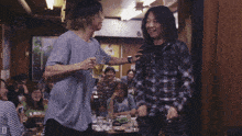 a man in a plaid shirt is pointing at another man in a crowded room