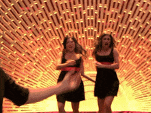 two women in black dresses are dancing in front of a wall of lines