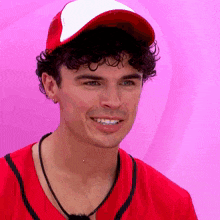 a man with curly hair wearing a red shirt and a baseball cap