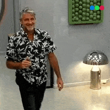 a man in a black and white shirt is standing in front of a lamp .