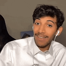 a man wearing ear buds and a white shirt is smiling and looking at the camera .