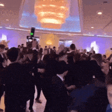 a crowd of people are dancing in a room with a large chandelier