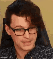 a man wearing glasses and a black and white polka dot shirt is sitting in a chair .