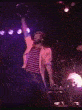 a man in a striped shirt is holding a microphone in the air on a stage