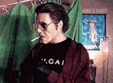 a man is smoking a cigarette in front of a green curtain while wearing sunglasses and a black shirt .