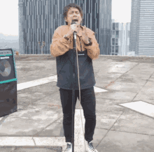 a man singing into a microphone on a rooftop with a speaker behind him