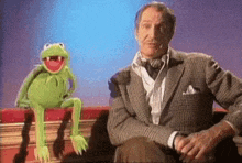 a man in a suit is sitting next to a kermit the frog puppet on a book .