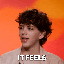 a man with curly hair says it feels in front of a red and orange background