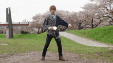 a man in a kimono stands in a park with cherry blossom trees in the background