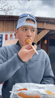 a man wearing sunglasses and a hat is eating a donut with a chopstick
