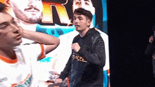 a man in a black hoodie is standing in front of a large screen with a picture of a man on it .