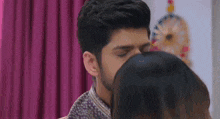a man and a woman are kissing in front of a mirror . the woman is wearing a purple saree .