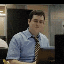 a man in a blue shirt and tie is sitting in front of a laptop .