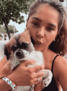 a woman in a black tank top is holding a small brown and white dog
