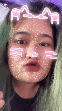 a girl with green hair is wearing a face mask with emojis on her face and the letters a and b on her forehead