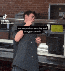 a man covering his face while standing in front of a subway