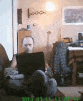 a man is sitting on a couch using a laptop with the date 2012 on the bottom right