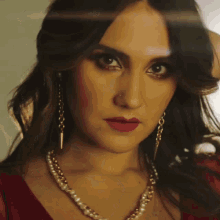 a woman wearing a pearl necklace and red lipstick looks at the camera