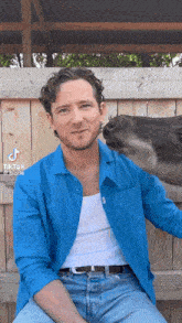 a man in a blue shirt is sitting next to a horse that is kissing his face .