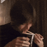 a man is eating noodles from a cup with a straw .