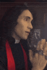 a man in a black shirt with a red scarf around his neck is talking on a cell phone