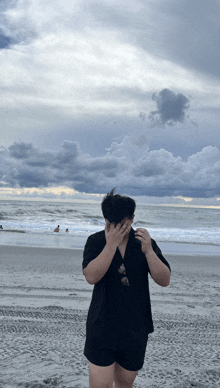 a person covering their face while standing on the beach