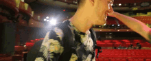 a man in a hawaiian shirt is standing in an auditorium with red seats