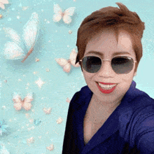 a woman wearing sunglasses and a blue shirt smiles in front of a blue background with butterflies