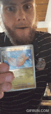 a man in a striped shirt is holding a pokemon card in front of a gifrun.com logo