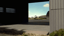 a plane is parked in a hangar with the door open and a shadow on the ground
