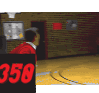 a man in a red shirt stands on a basketball court with a sign that says 350