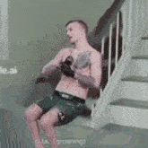a shirtless man is sitting on a staircase holding a cell phone .