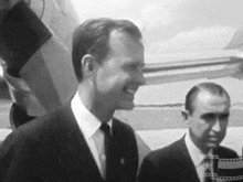 a man in a suit and tie is smiling in front of a plane
