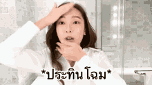a woman in a white shirt is looking at her face in a bathroom with a foreign language written on the bottom