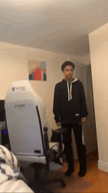 a man in a black hoodie is standing in front of a white chair in a room .