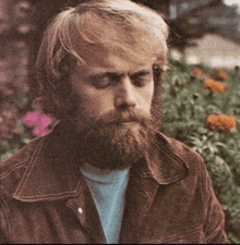 a man with a beard wearing a brown jacket and a blue shirt