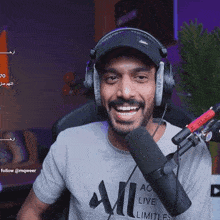 a man wearing headphones and a shirt that says " all " is smiling in front of a microphone