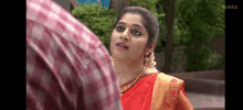 a woman in a red saree is standing next to a man in a plaid shirt .