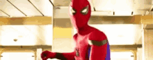 a man in a spiderman costume is standing in a room with a fist in the air .