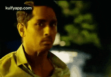 a man in a yellow shirt is standing in front of a car .