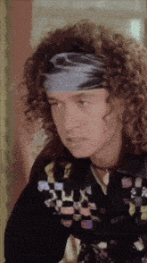 a man with curly hair is wearing a headband and a checkered jacket