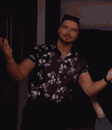 a man wearing a black floral shirt is standing in a dark room