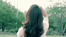 a woman with long black hair is standing in a park holding her hair in her hand .