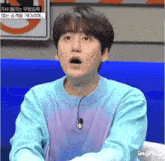 a man in a blue sweater with a microphone around his neck is making a funny face