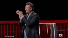 a man in a suit applauds while sitting in front of a nbc podium